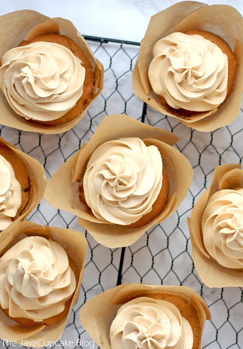 Perfect Peanut Butter Buttercream Frosting swirled onto cupcakes in brown liners sitting on a black cooling rack