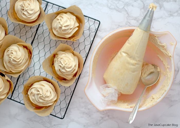 Perfect Peanut Butter frosting in a piping bag alongside of Peanut Butter Cupcakes