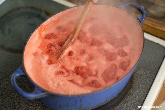Strawberries boiling in a blue pot, there is foam on the top, caused by the natural pectin 