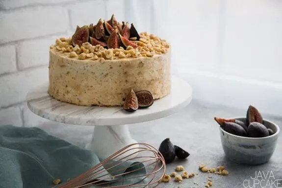 cake topped with figs and hazelnuts on a white background with a bowl of figs