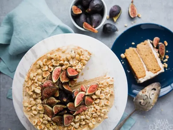 fig and hazelnut cake on a stand with a slice of cake on a plate and a bowl of figs