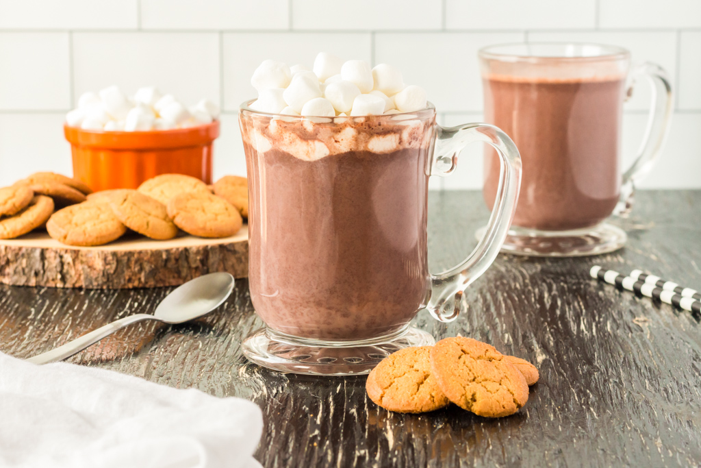 homemade hot chocolate in a glass mug on a counter with cookies