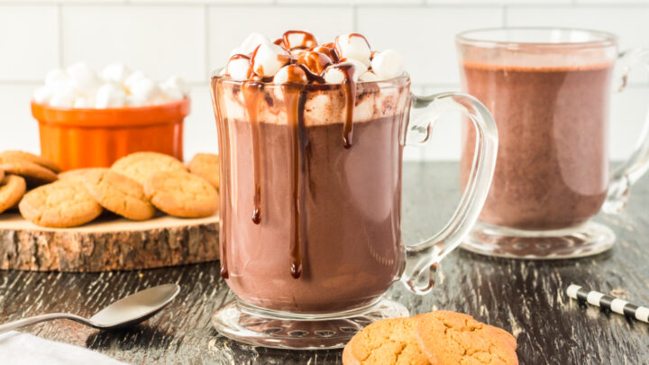 a glass mug full of hot chocolate topped with marshmallows and fudge
