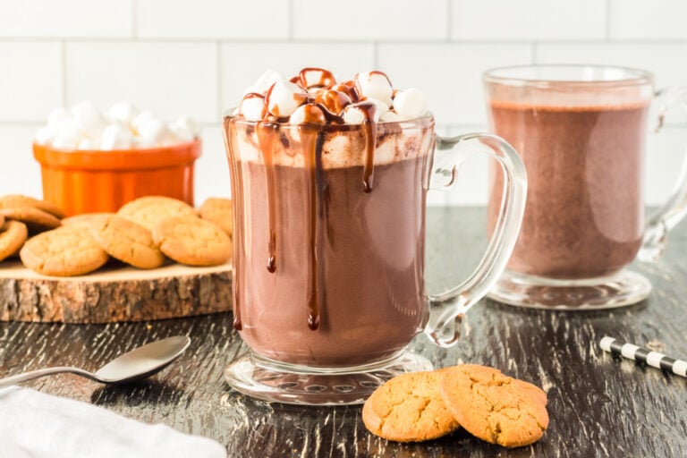 a glass mug full of hot chocolate topped with marshmallows and fudge