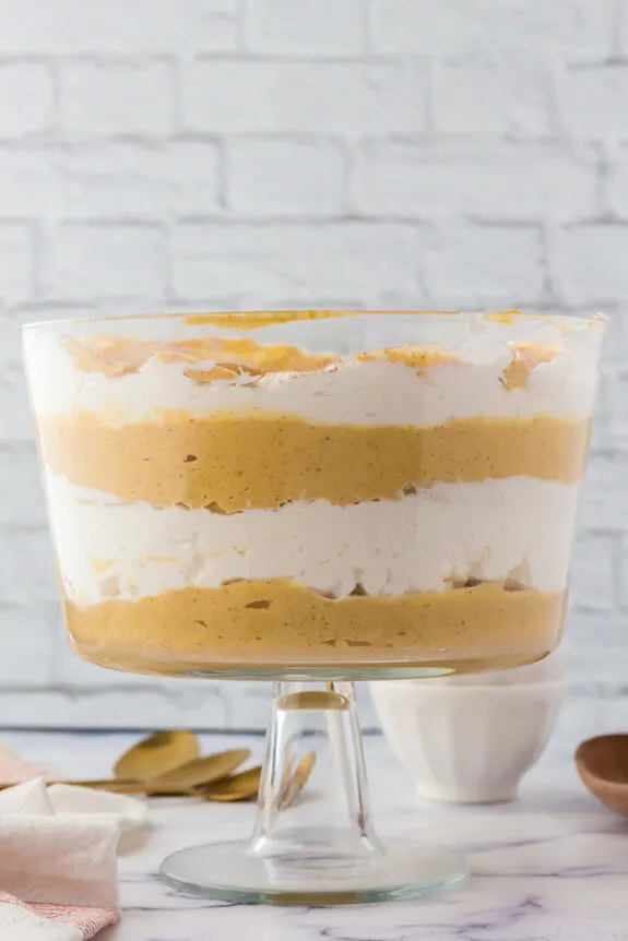 In a white kitchen, a glass trifle dish holds the easy pumpkin cream trifle. The view is side on so you can see the different layers of pumpkin pudding and fresh whipped cream.