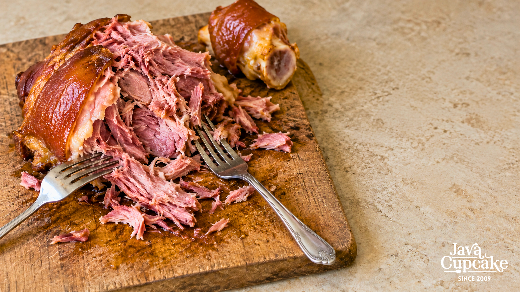 Tender smoked ham hock pulled apart with forks on a wooden cutting board.