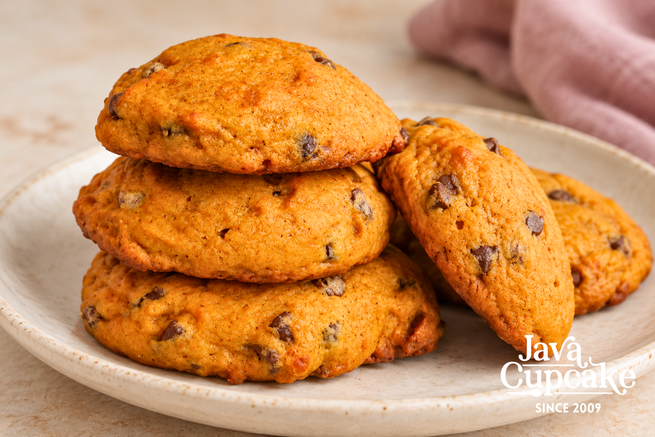 Thick pumpkin chocolate chip cookies stacked and leaning together on a cream plate.
