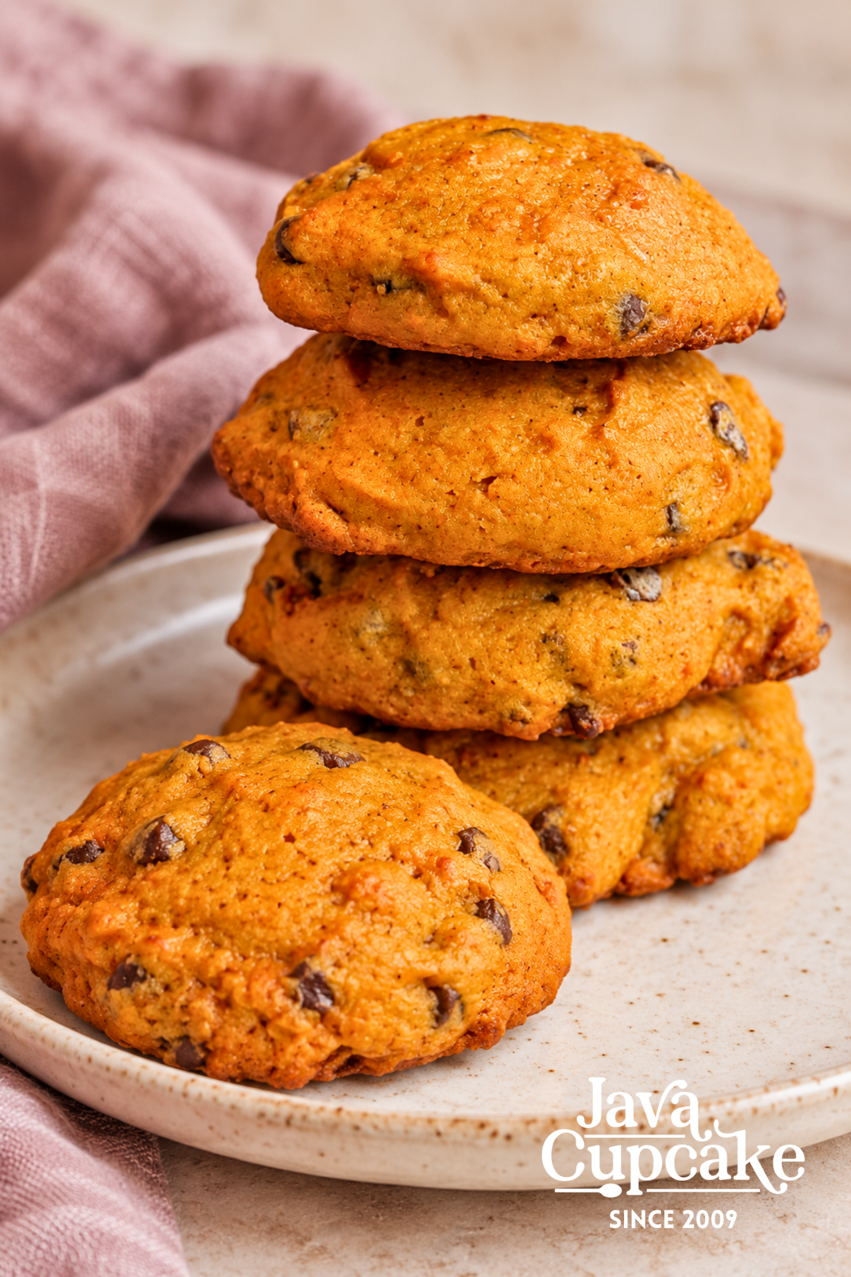 Soft pumpkin chocolate chip cookies stacked on a cream plate beside mauve linen