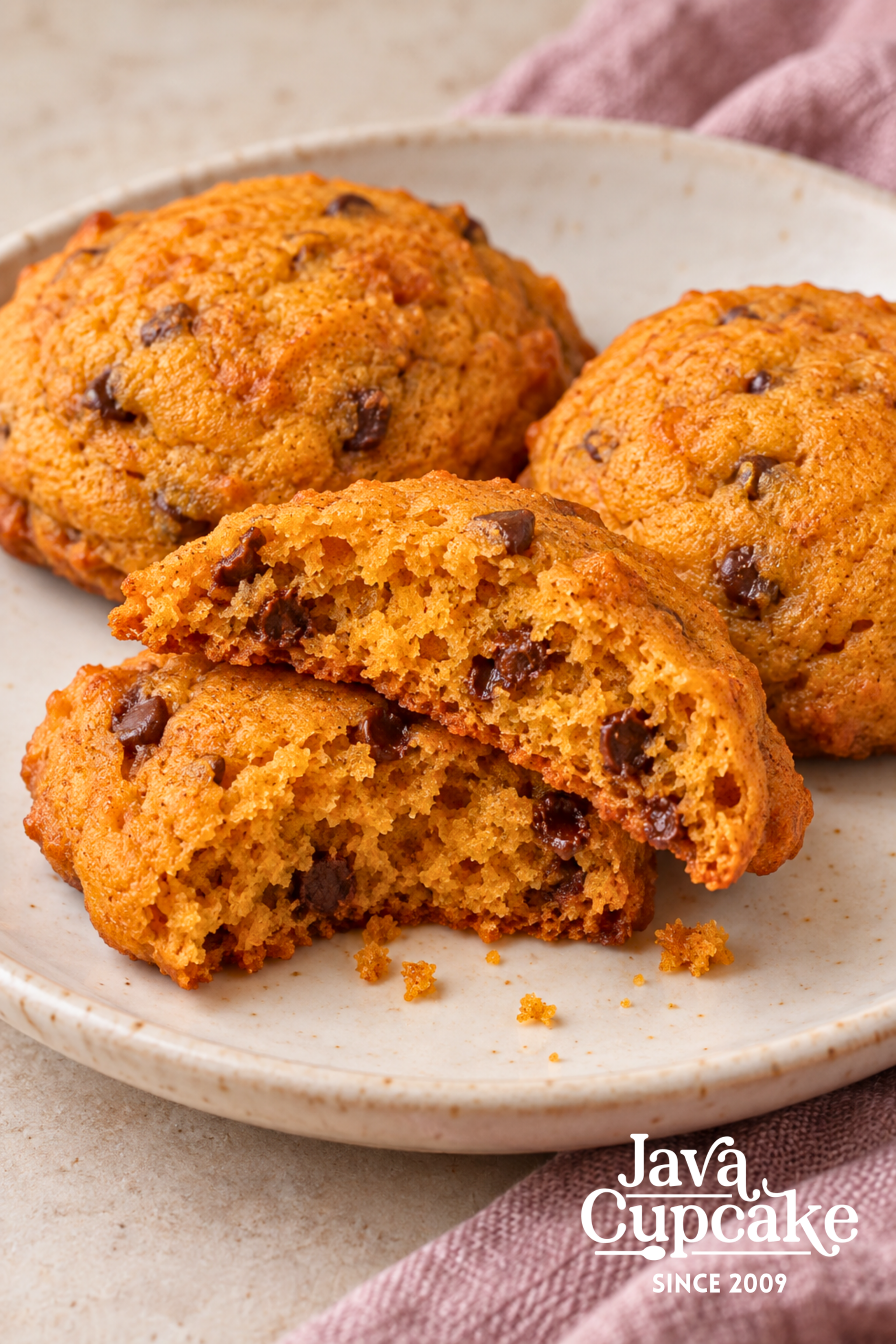 A pumpkin chocolate chip cookie broken open to show its soft orange crumb and chocolate chips.
